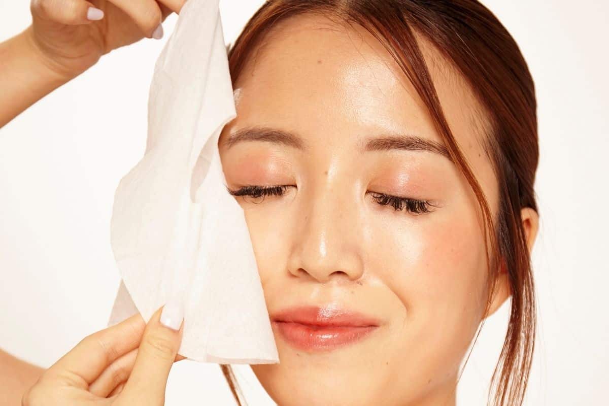 Woman with closed eyes removing a sheet mask from her face.